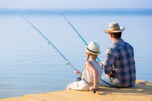 Father and daughter sitting on dock fishing.