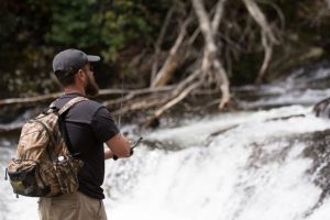 Man fishing in a river while wearing a backpack